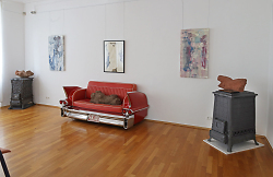 Auf dem Bild ist ein rotes Sofa im Stil eines amerikanischen 50er-Jahre-Autos zu sehen. Darauf liegt ein Torso als Ausstellungsstück. An den Seiten sind nochmals zwei Torsos ausgestellt