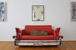 Auf dem Bild ist ein rotes Sofa im Stil eines amerikanischen 50er-Jahre-Autos zu sehen. Darauf liegt ein Torso als Ausstellungsstück.
