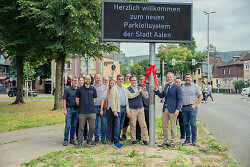 Auf dem Bild ist Oberbürgermeister Frederick Brütting (3.v.re.) freut sich gemeinsam mit Erstem Bürgermeister Wolfgang Steidle (5.v.re.), Mitgliedern des Gemeinderats sowie Projektbeteiligten der Stadtverwaltung über den Start des neuen Parkleitsystems zu sehen.